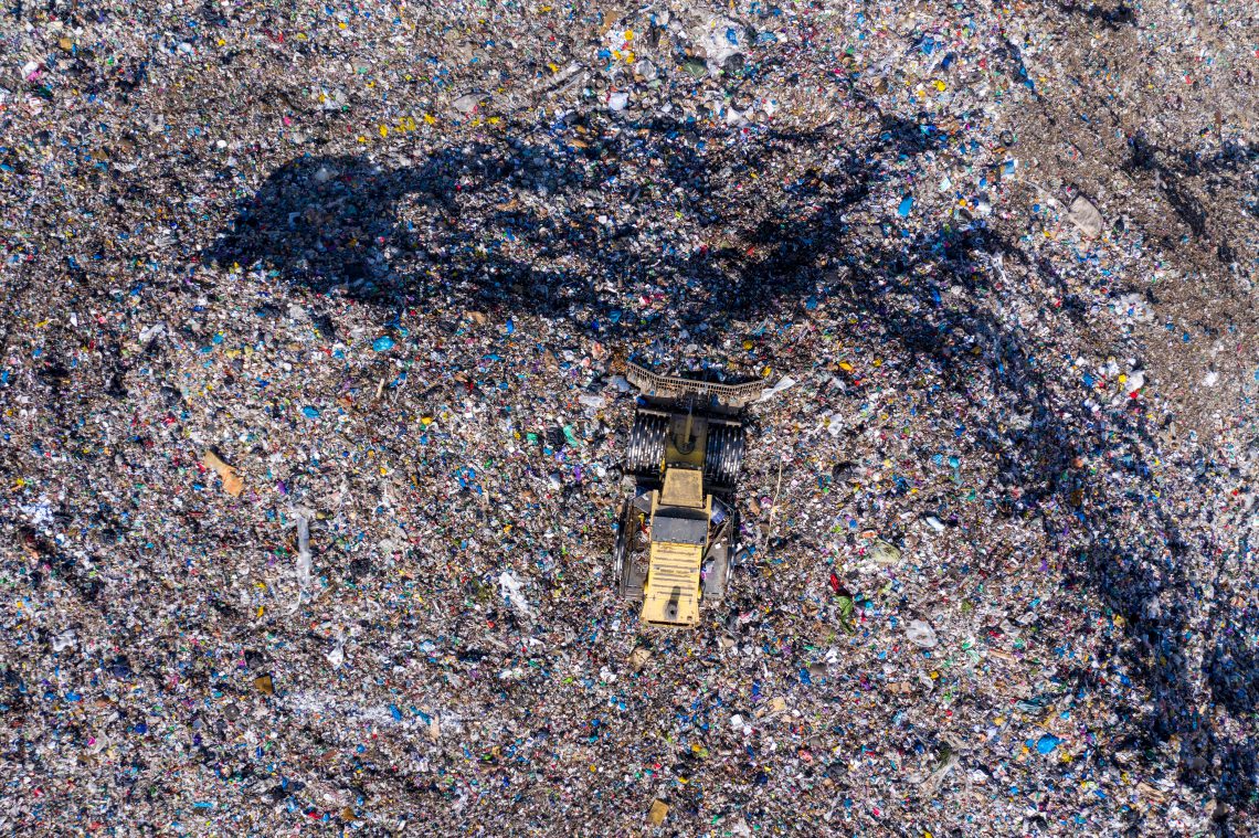 Aerial top drone view of large garbage pile, trash dump, landfill, waste from household dumping site, excavator machine is working on a mountain of garbage.